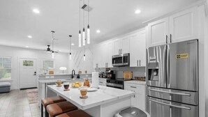 A modern kitchen with white cabinets, stainless steel appliances, and a central island with stools. - 612 New Construction Fire Pit Games (Houston)