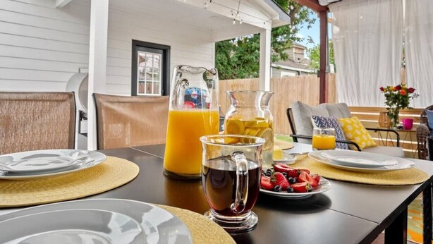 An outdoor dining area with a table set for breakfast, including a pitcher of orange juice, a pitcher of iced tea, and a plate of fresh fruit. - 612 New Construction Fire Pit Games (Houston)