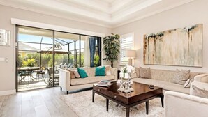 Ein geräumiges Wohnzimmer mit einer großen Glasschiebetür, die auf eine Außenpatio führt, ein beiges Sofa mit türkisfarbenen Kissen, ein dunkles Holz-Couchtisch und ein großes abstraktes Gemälde an der Wand.