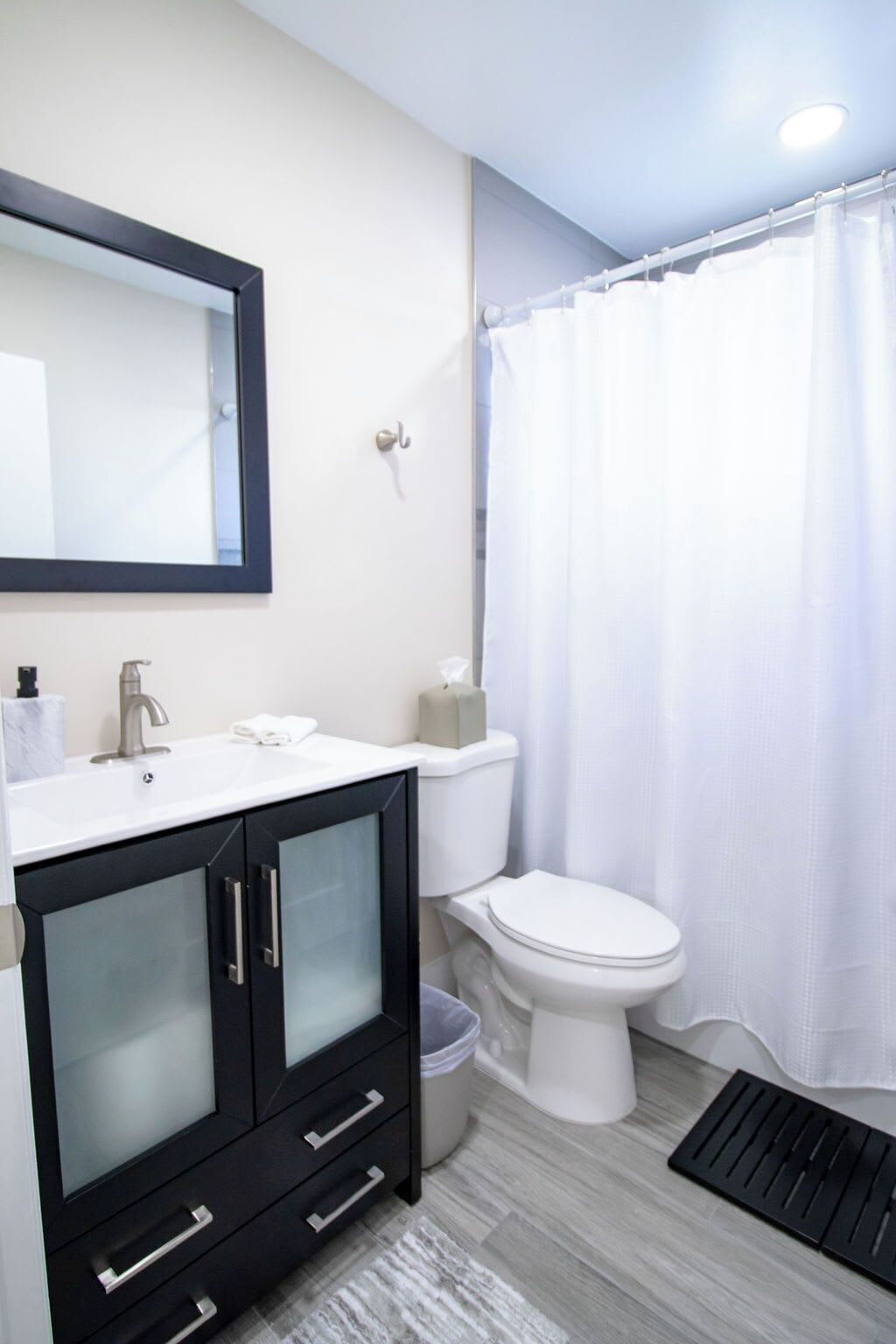 Un baño con lavamanos blanco, espejo, inodoro y cortina de ducha.