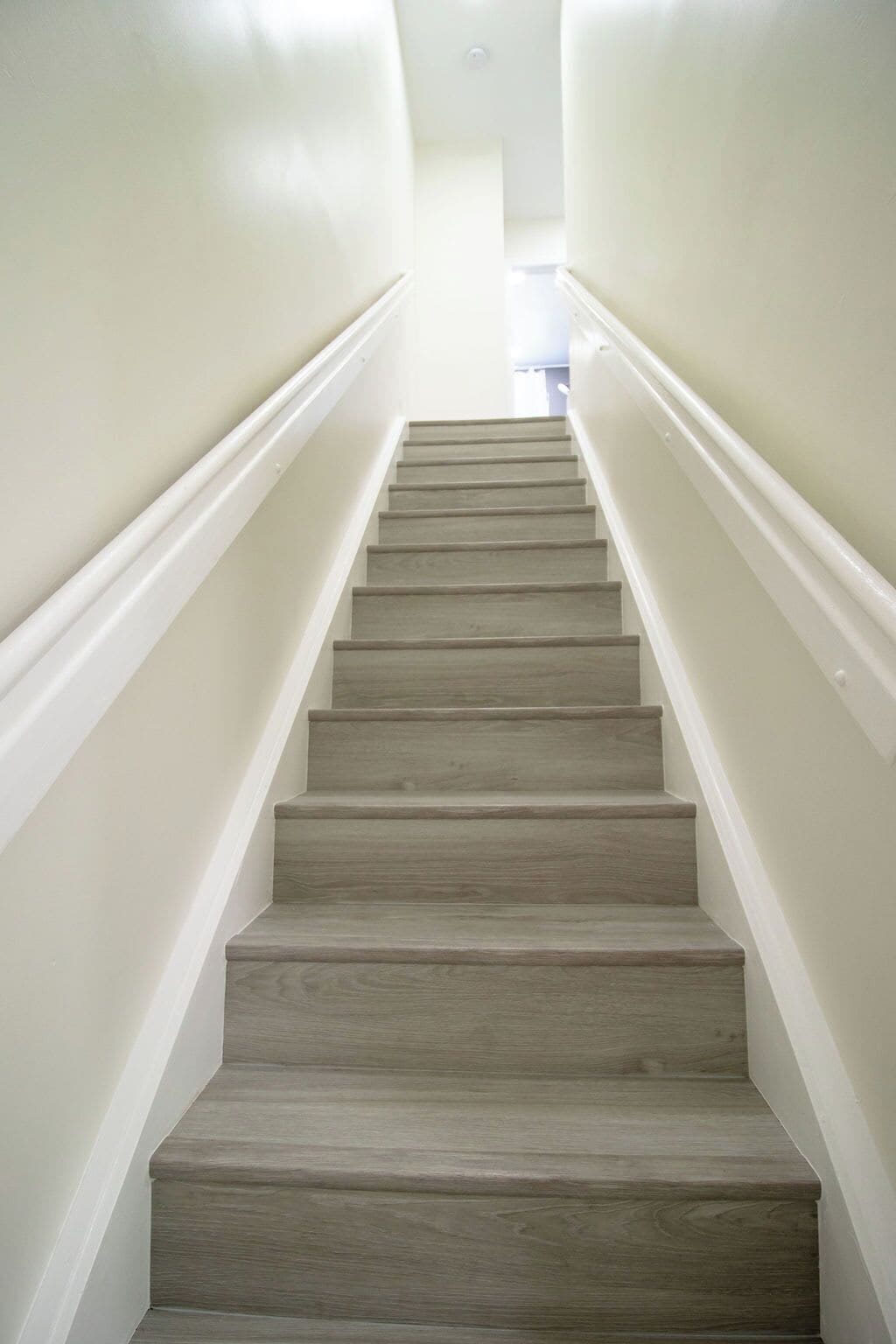 Een trap met een licht houten afwerking, witte wanden en een recht, smal ontwerp.