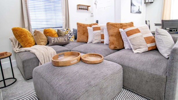 A modern living room with a grey sectional sofa, wooden trays, and a 'FAMILY' pillow. - Good Vibes Oasis - Cozy Townhome With Parking (Cutler Bay)
