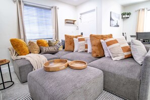 A modern living room with a grey sectional sofa, wooden trays, and a 'FAMILY' pillow.