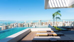Une piscine sur le toit avec vue sur la ville, des chaises longues et un petit palmier.