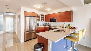 A modern kitchen with stainless steel appliances, wooden cabinets, and a bar area with stools. - Hang Ten- Large Townhome, lux Amenities, Parking (Miami)