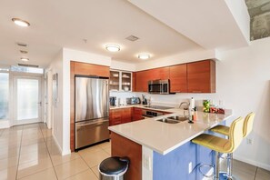 A modern kitchen with stainless steel appliances, wooden cabinets, and a bar area with stools. - Hang Ten- Large Townhome, lux Amenities, Parking (Miami)