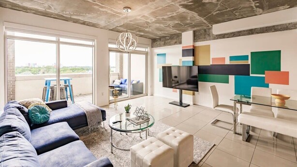 A modern living room with a sofa, a glass coffee table, a TV, and a dining area with a glass table and chairs. - Hang Ten- Large Townhome, lux Amenities, Parking (Miami)