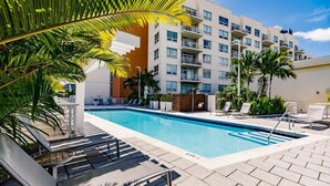 A swimming pool with lounge chairs, a building with balconies, and palm trees. - Hang Ten- Large Townhome, lux Amenities, Parking (Miami)