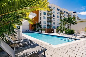 A swimming pool with lounge chairs, a building with balconies, and palm trees. - Hang Ten- Large Townhome, lux Amenities, Parking (Miami)