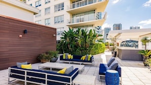 An outdoor seating area with sofas and tables, surrounded by greenery and a cityscape in the background. - Hang Ten- Large Townhome, lux Amenities, Parking (Miami)