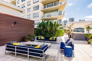 An outdoor seating area with sofas and tables, surrounded by greenery and a cityscape in the background. - Hang Ten- Large Townhome, lux Amenities, Parking (Miami)