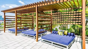 A rooftop lounge with wooden pergolas, blue cushioned seating, and a backdrop of greenery. - Hang Ten- Large Townhome, lux Amenities, Parking (Miami)
