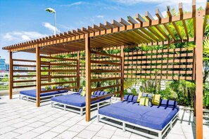 A rooftop lounge with wooden pergolas, blue cushioned seating, and a backdrop of greenery. - Hang Ten- Large Townhome, lux Amenities, Parking (Miami)