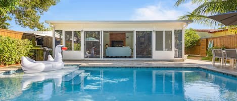 Une piscine avec un flotteur en forme de cygne, un patio couvert et une vue sur le jardin arrière.
