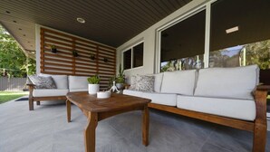 A modern outdoor living area with a wooden table, two white sofas, and a large window. - Boho House - Stylist Home With a Large Yard (Miami)