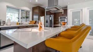 A modern kitchen with a central island, stainless steel appliances, and yellow bar stools. - Boho House - Stylist Home With a Large Yard (Miami)