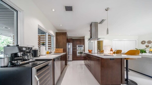 A modern kitchen with a central island, built-in appliances, and a large window. - Boho House - Stylist Home With a Large Yard (Miami)