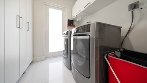 A laundry room with two washing machines, a red drying rack, and white cabinetry. - Boho House - Stylist Home With a Large Yard (Miami)