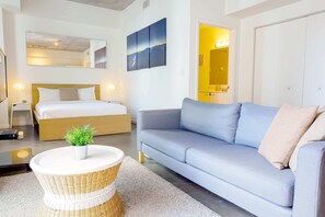 Een moderne hotelkamer met een bed, een bank, een rond rieten tafeltje en een potplant.