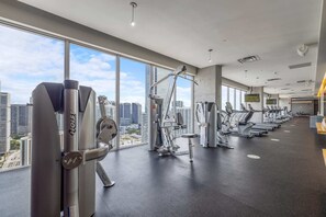 A gym with various exercise machines, large windows, and a city view. - Cozy Downtown Pad- Luxe Rooftop Pool, gym and More (Miami)