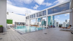 An indoor swimming pool with a city view, lounge chairs, and a modern architectural design.