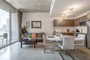 A modern apartment with a dining area, kitchen, and a large window with a city view. - Cozy Downtown Pad- Luxe Rooftop Pool, gym and More (Miami)