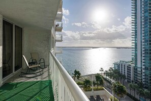 A balcony with a view of the sea, a high-rise building, and a clear sky. - Brickell Bay View- Unbeatable Location With Parking (Miami)