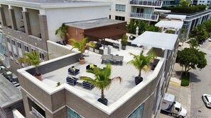 Une terrasse sur le toit, avec des espaces de détente en plein air, des palmiers et un bâtiment moderne en arrière-plan.