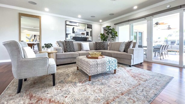 Ein modernes Wohnzimmer mit grauem Sofa, einem gemusterten Pouf und einem grauen Sessel.