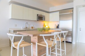 A modern kitchen with white cabinets, a central island with stools, a stainless steel refrigerator, and a microwave. - Brickell House Dreams - Luxury Stay and Amenities (Miami)