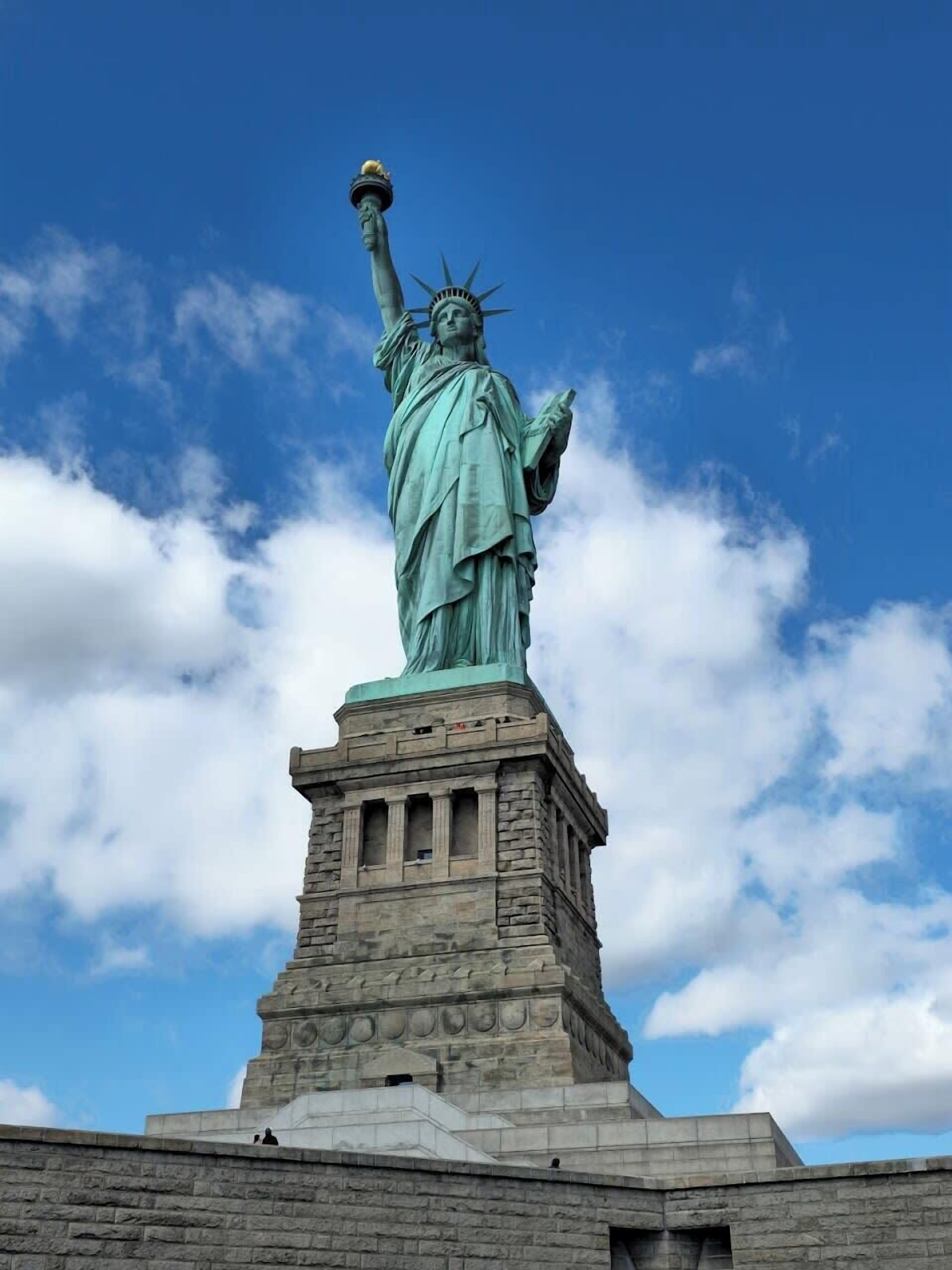 A statue of a woman holding a torch and a tablet, standing on a stone pedestal.