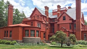 A large, red brick building with multiple chimneys, a stone foundation, and a well-maintained garden. - Serene Stay With Amenities & Breakfast bar (West Orange)