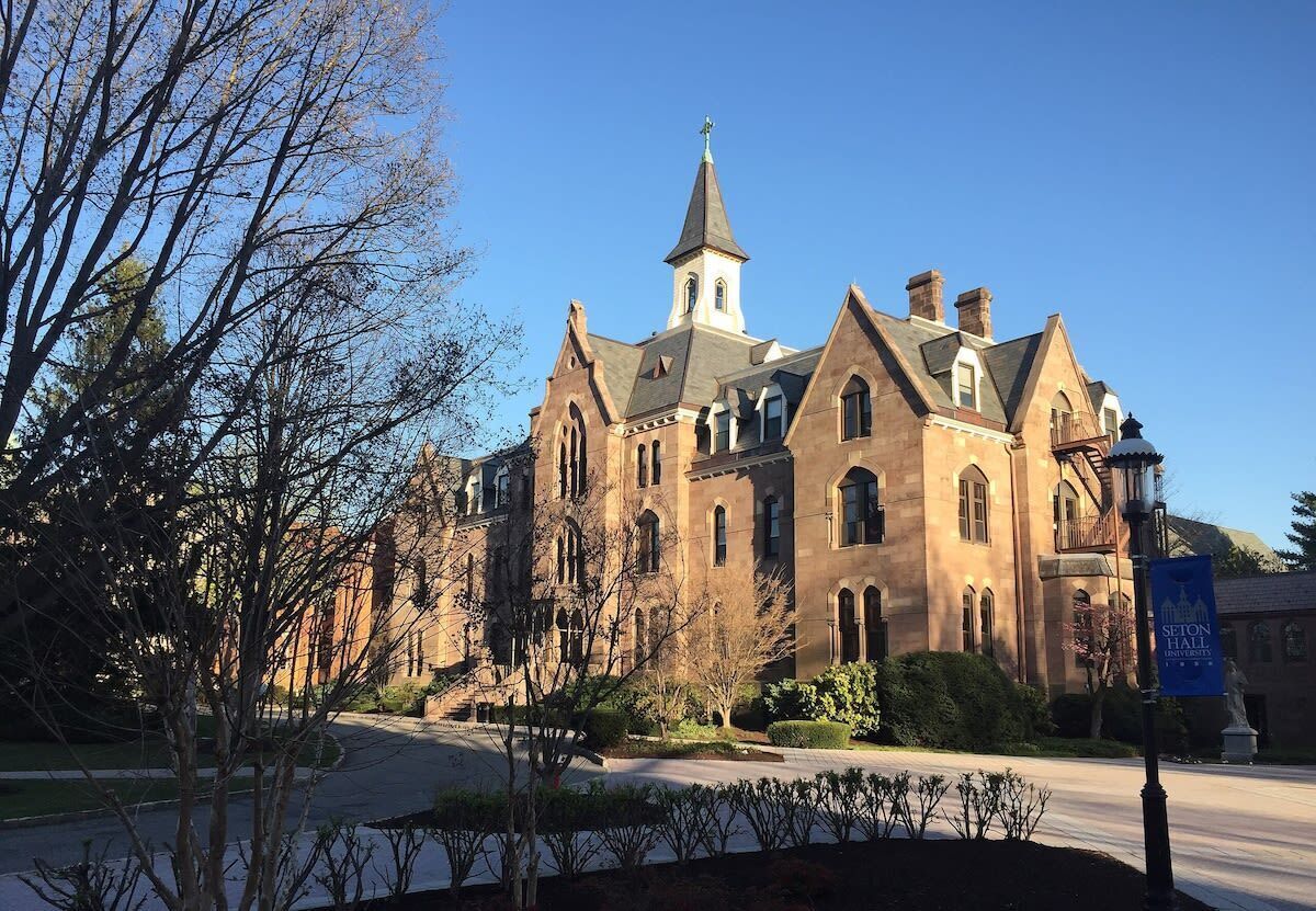 A large, historic building with a prominent tower and arched windows, surrounded by well-maintained landscaping.