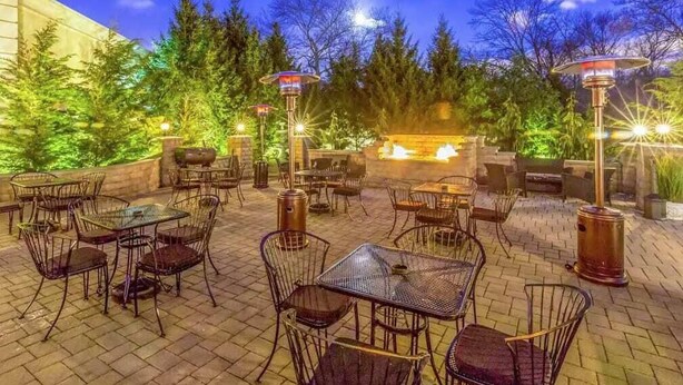 An outdoor patio area with tables and chairs, surrounded by trees and a fire feature. - Serene Stay With Amenities & Breakfast bar (West Orange)