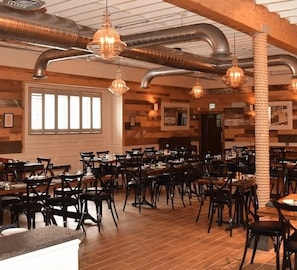 A restaurant with wooden walls, metal ductwork, and hanging pendant lights. Tables are set with chairs. - Serene Stay With Amenities & Breakfast bar (West Orange)