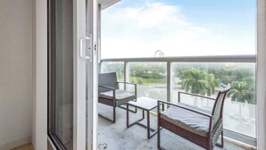 A balcony with a view of greenery and buildings, a metal-framed chair, a small table, and a wicker chair. - Biscayne Bay Views-pool, Hot Tub and Amenities (Miami)