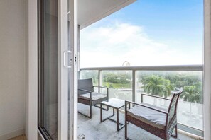 A balcony with a view of greenery and buildings, a metal-framed chair, a small table, and a wicker chair. - Biscayne Bay Views-pool, Hot Tub and Amenities (Miami)