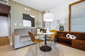 A modern living room with a sofa, two chairs, a round table, a floor lamp, a large abstract painting, and a wooden cabinet with decorative items. - Biscayne Bay Views-pool, Hot Tub and Amenities (Miami)