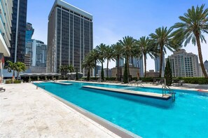 A swimming pool with lounge chairs, palm trees, and tall buildings in the background. - Biscayne Bay Views-pool, Hot Tub and Amenities (Miami)