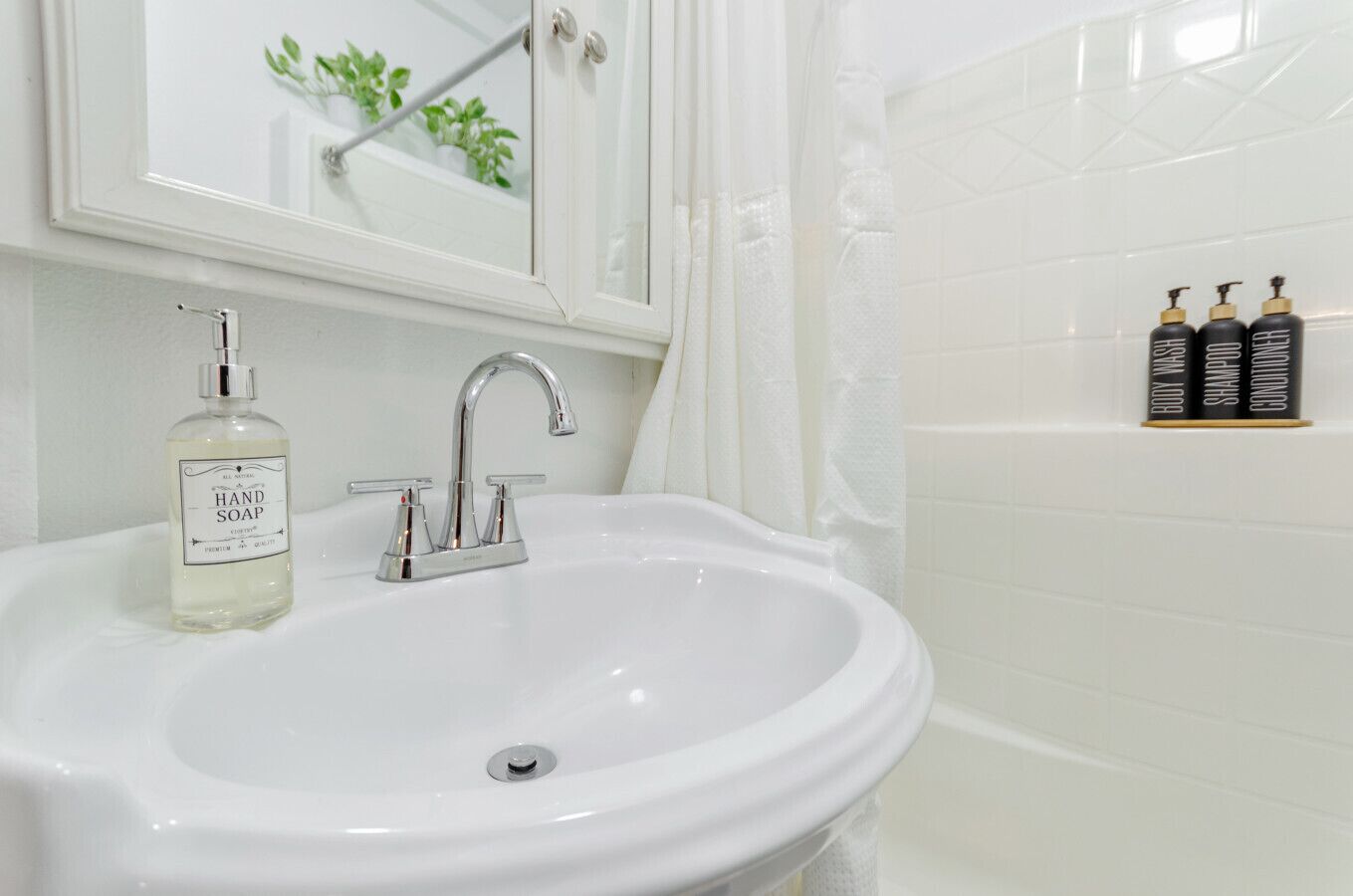 Ein weißes Waschbecken mit chromfarbenem Wasserhahn, eine Handseifenflasche und Toilettenartikel an der Wand.