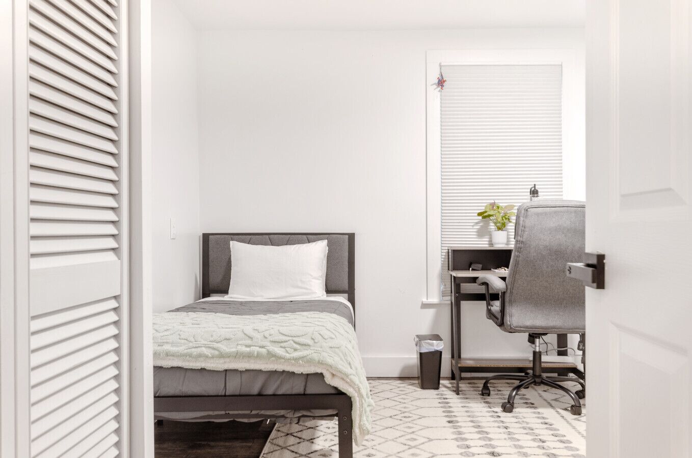 A bedroom with a bed, a desk, and a chair.