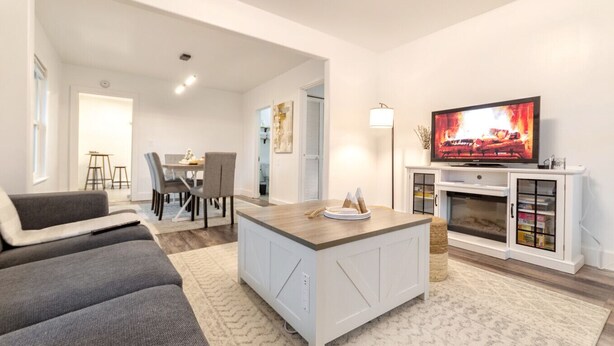 A modern living room with a sofa, a dining area with chairs, a TV, and a fireplace. - Zen Retreat Near Tacoma & Seattle (Tacoma)