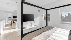 Ett modernt sovrum med en stor säng, en tv som är monterad på väggen och utsikt över staden genom fönstret.