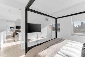 A modern bedroom with a large bed, a TV mounted on the wall, and a city view through the window. - Skyline Lux Escape Midtown Manhattan High-rise! (New York)