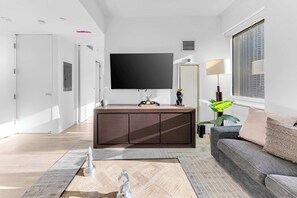 Un salón moderno con televisión de pantalla plana, mueble bajo de madera oscura, sofá gris y un ventanal grande.
