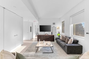 A modern living room with a flat-screen TV, a sofa, a coffee table, and a large window with a city view. - Skyline Lux Escape Midtown Manhattan High-rise! (New York)