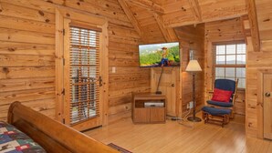 A wooden cabin room with a bed, a TV mounted on the wall, a chair, and a lamp. - 492a) Mountain View 4BR With Hot Tub! (Sevierville)