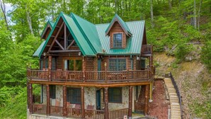 A log cabin with a green roof, a balcony, and a stone foundation. - 492a) Mountain View 4BR With Hot Tub! (Sevierville)