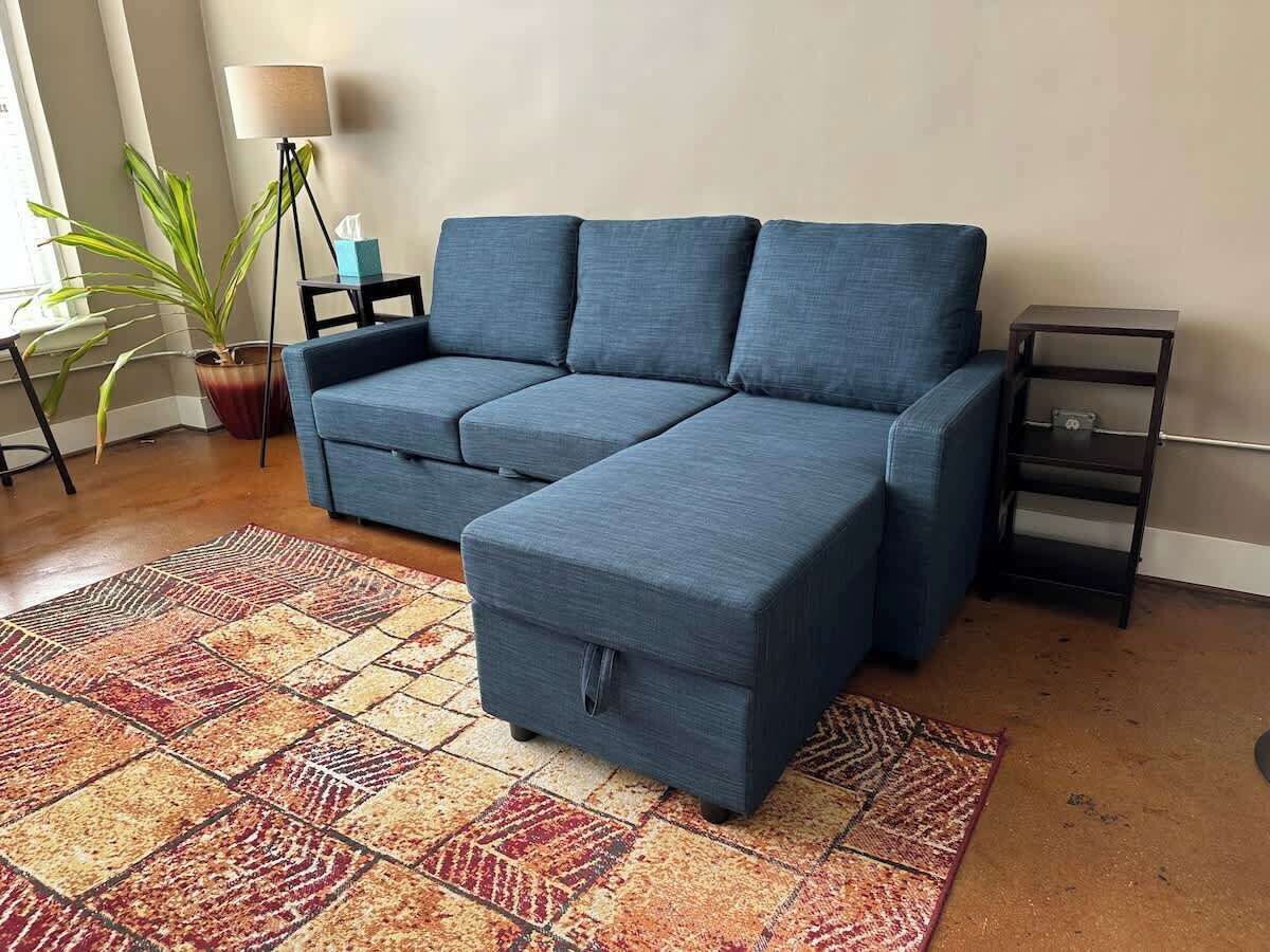 Un canapé modulable assorti d’un pouf, un tapis à motifs, une lampe sur pied et une petite table avec une plante.