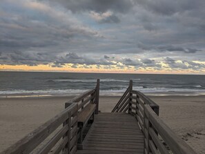 Ein hölzerner Steg führt zu einem Strand mit Wellen und bewölktem Himmel.